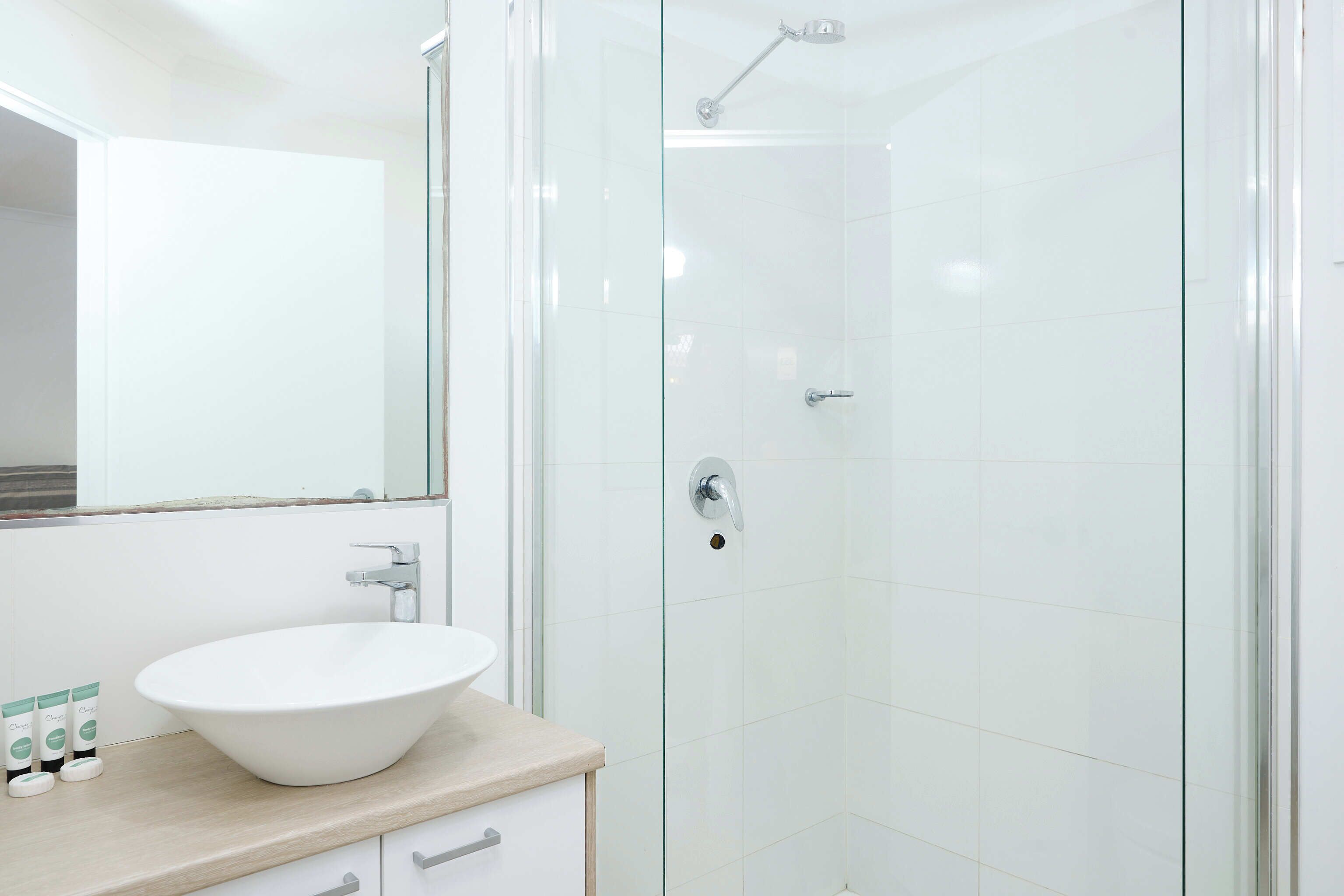 Ein modernes Badezimmer mit einem weißen Waschbecken, einer Duschkabine aus Glas und einem großen Spiegel.