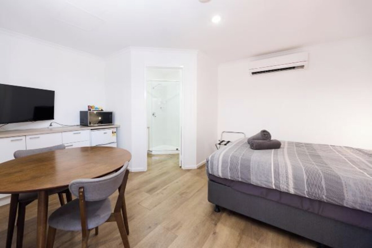 A modern bedroom with a bed, a TV, a desk, and a shower.