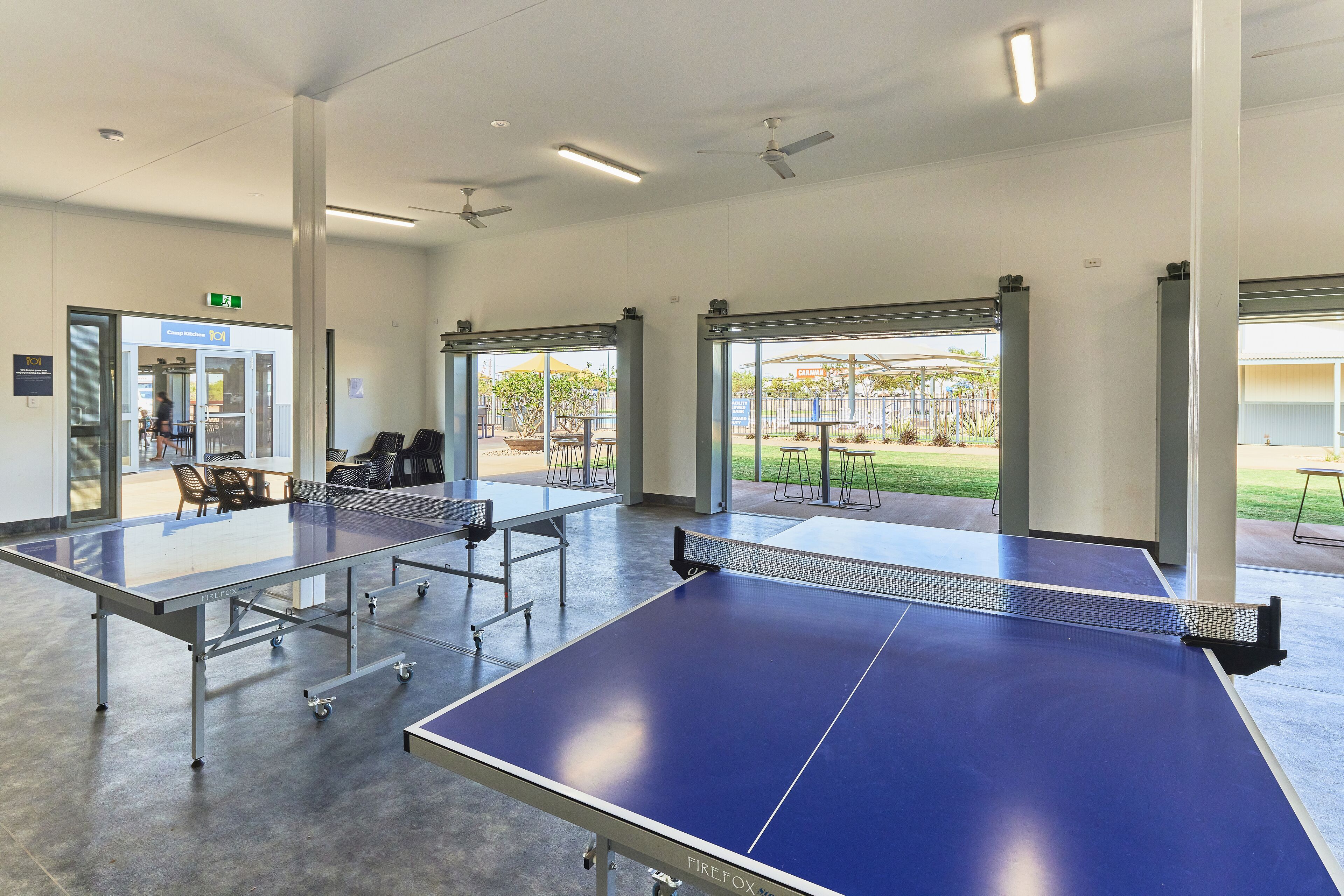 A spacious indoor area with ping pong tables, a door leading outside, and a view of a garden.