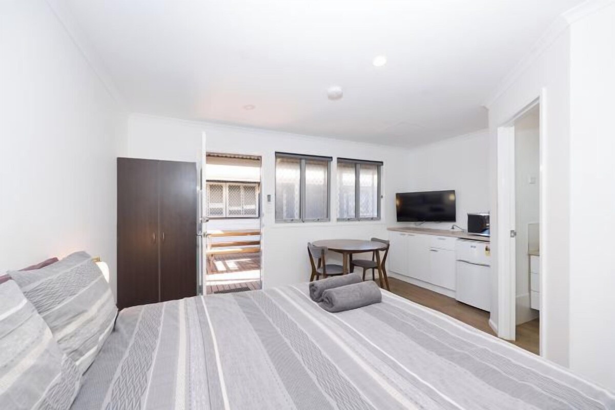 Une chambre compacte comprenant un lit, un petit bureau, une télévision et un coin cuisine.