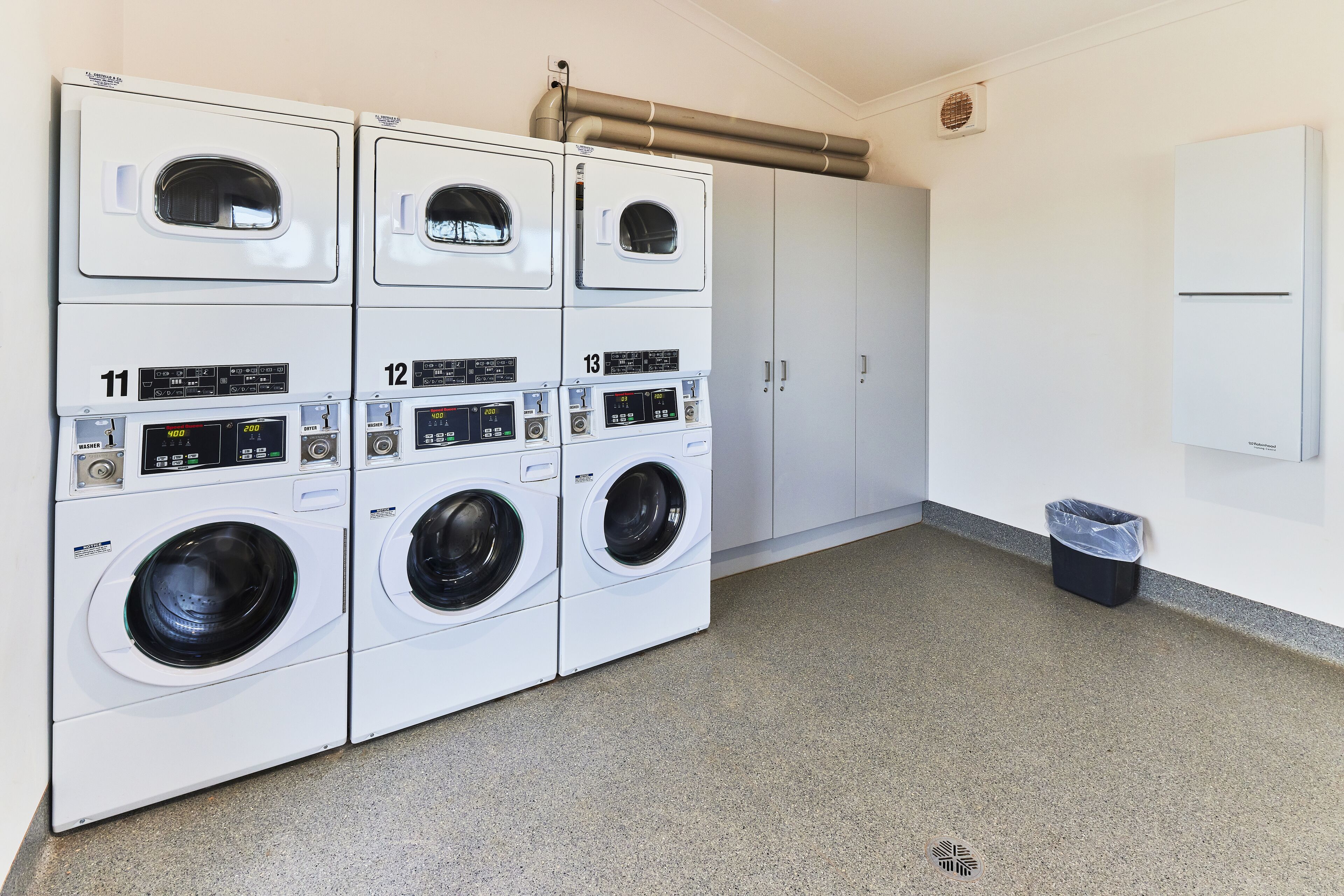 A laundry facility with three stacked washing machines, numbered 11, 12, and 13, and a single dryer.