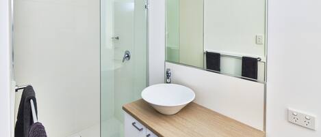 Une salle de bain moderne avec une douche à parois de verre, un lavabo blanc doté d’un plan de toilette en bois et un miroir au-dessus du lavabo.