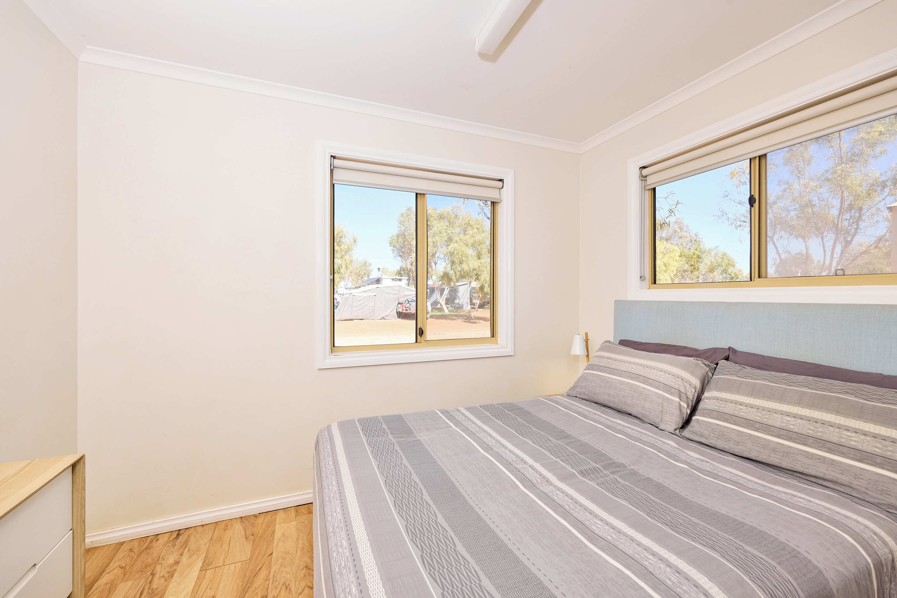 A bedroom with a bed, two windows, and a wooden floor.