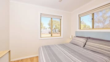 A bedroom with a bed, two windows, and a wooden floor.