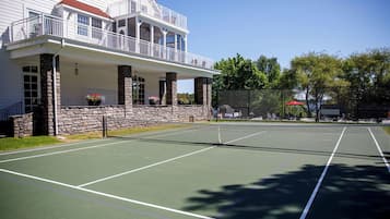 A tennis court with a stone wall and a white building with a balcony.