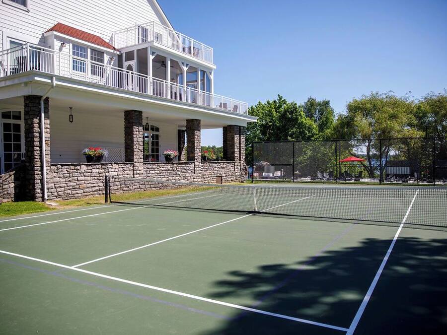 A tennis court with a stone wall and a white building with a balcony.