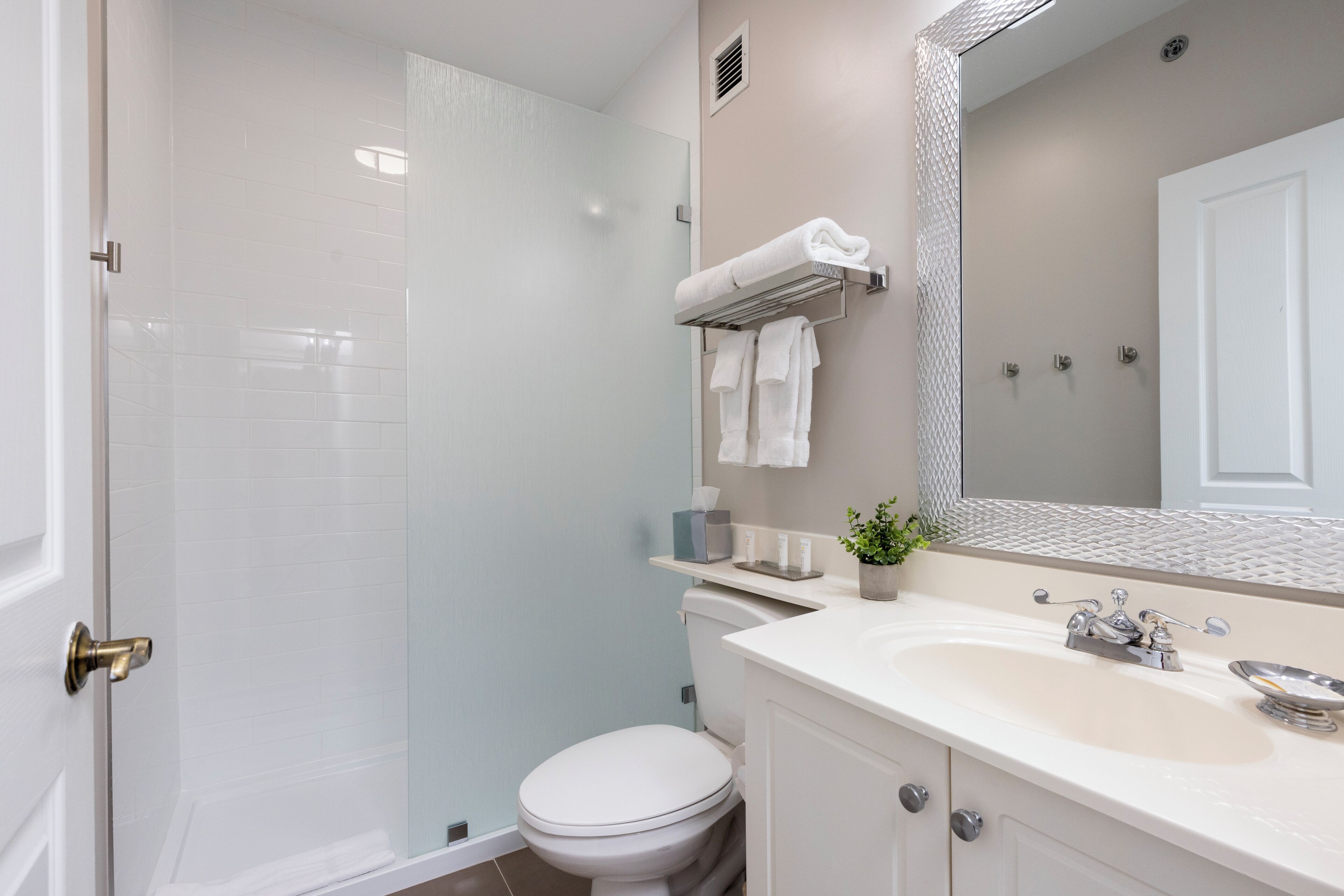 Un baño moderno con cabina de ducha de vidrio, inodoro blanco, tocador con lavabo y espejo sobre el lavabo.