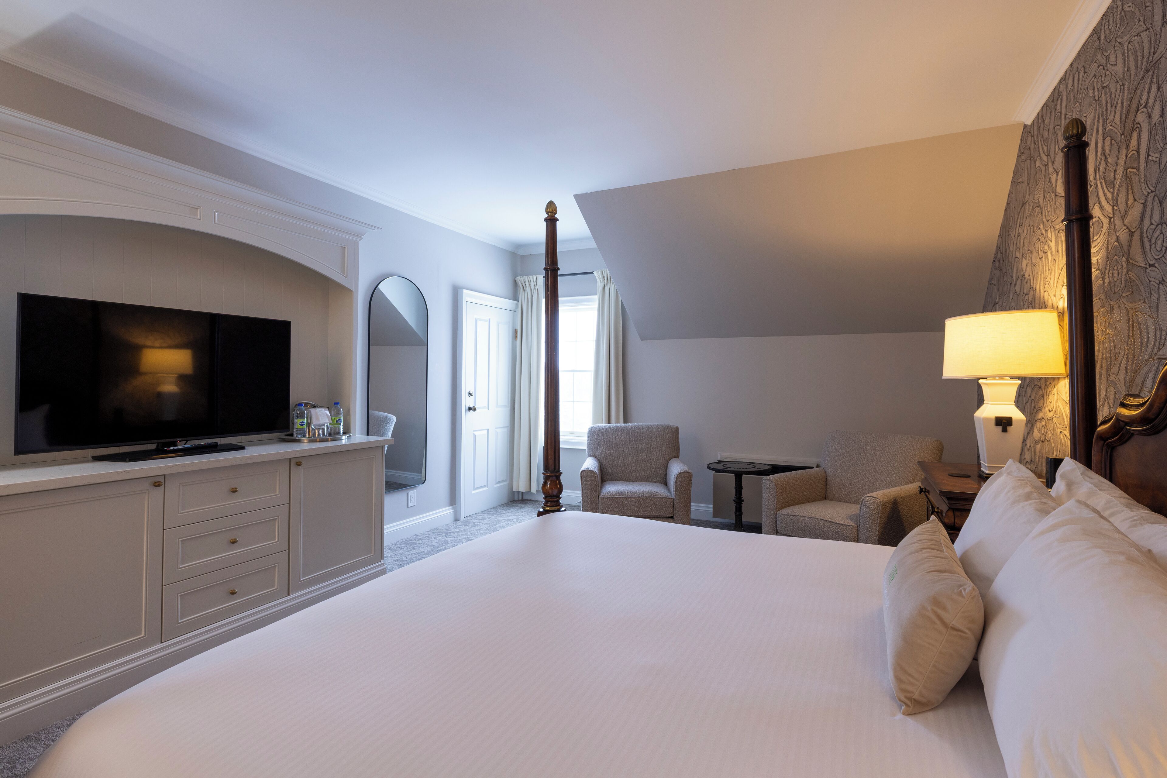 A hotel room with a large bed, a television, a desk, and a chair.