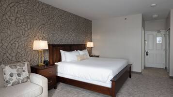 Habitación de hotel ordenada con una cama grande, dos mesitas de noche con lámparas, una mesita auxiliar de madera y un papel tapiz con estampado floral.