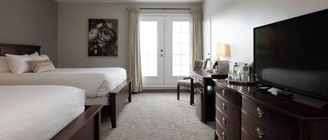 A hotel room with two beds, a desk with a television, and a painting on the wall.
