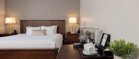 A hotel room with a wooden bed, two bedside lamps, a nightstand with a lamp, a tray with a coffee maker, a framed picture, and a potted plant.