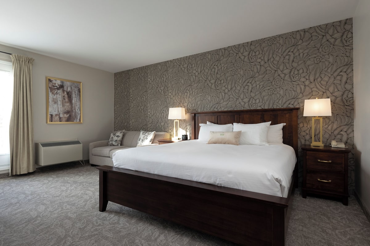 Une chambre d’hôtel avec un grand lit, deux tables de chevet avec des lampes, un canapé, un radiateur et un papier peint à motifs.