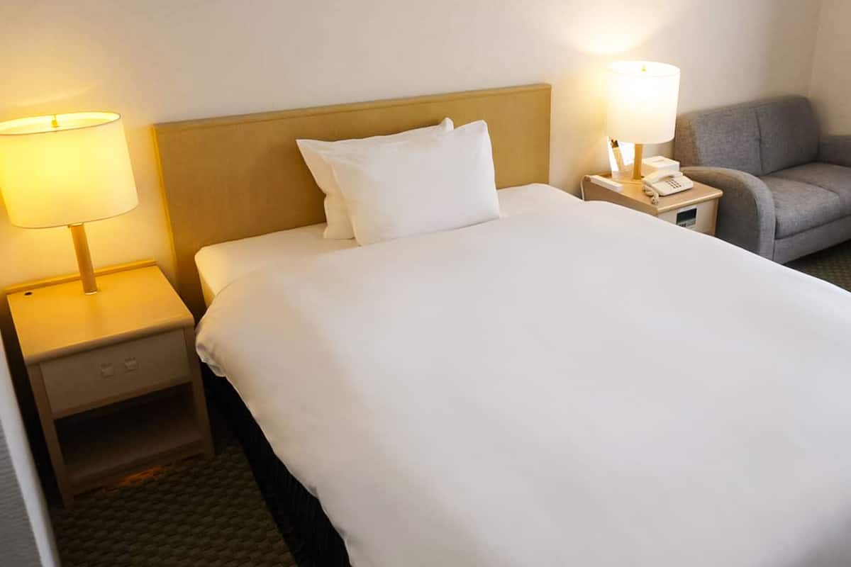 Una habitación de hotel con una cama grande, dos lámparas de noche, una silla, una mesita y un teléfono.