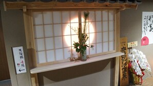 A traditional Japanese room with a shoji screen, a wooden shelf with a vase of flowers, and a sign indicating the direction to the bathroom. - Kobe PortTower Hotel (Kobe)