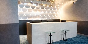 Un comptoir d’accueil au design moderne, doté d’un plateau de couleur claire et de deux tables en verre avec des supports noirs.