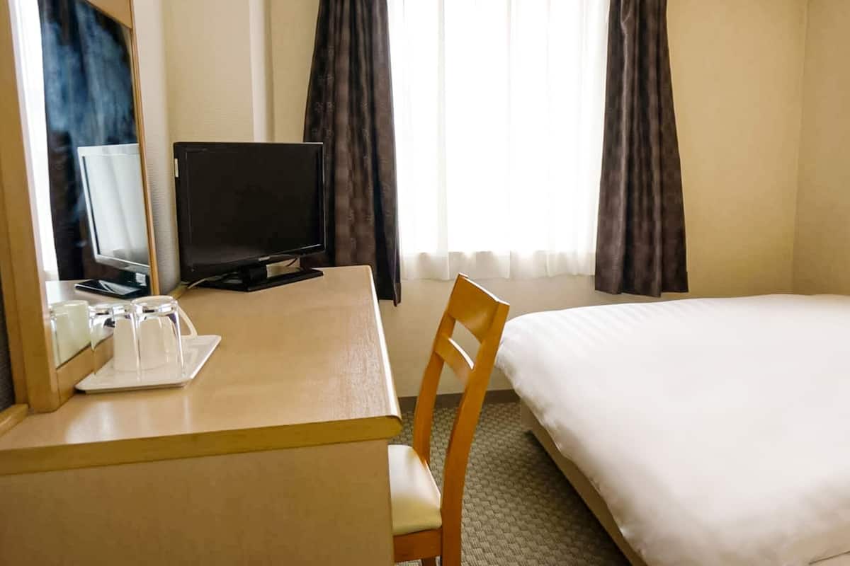 Habitación de hotel con cama, escritorio con computadora y silla, y ventana con cortinas.