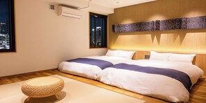 A neatly arranged hotel room with a large bed, a window with a city view, a wall-mounted air conditioner, and a woven floor mat. - Kobe PortTower Hotel (Kobe)