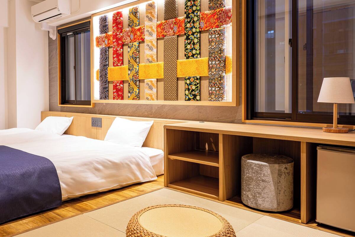 Habitación de hotel con dos camas, un ventanal grande, un toallero en la pared, un escritorio de madera y un cubo de basura pequeño.