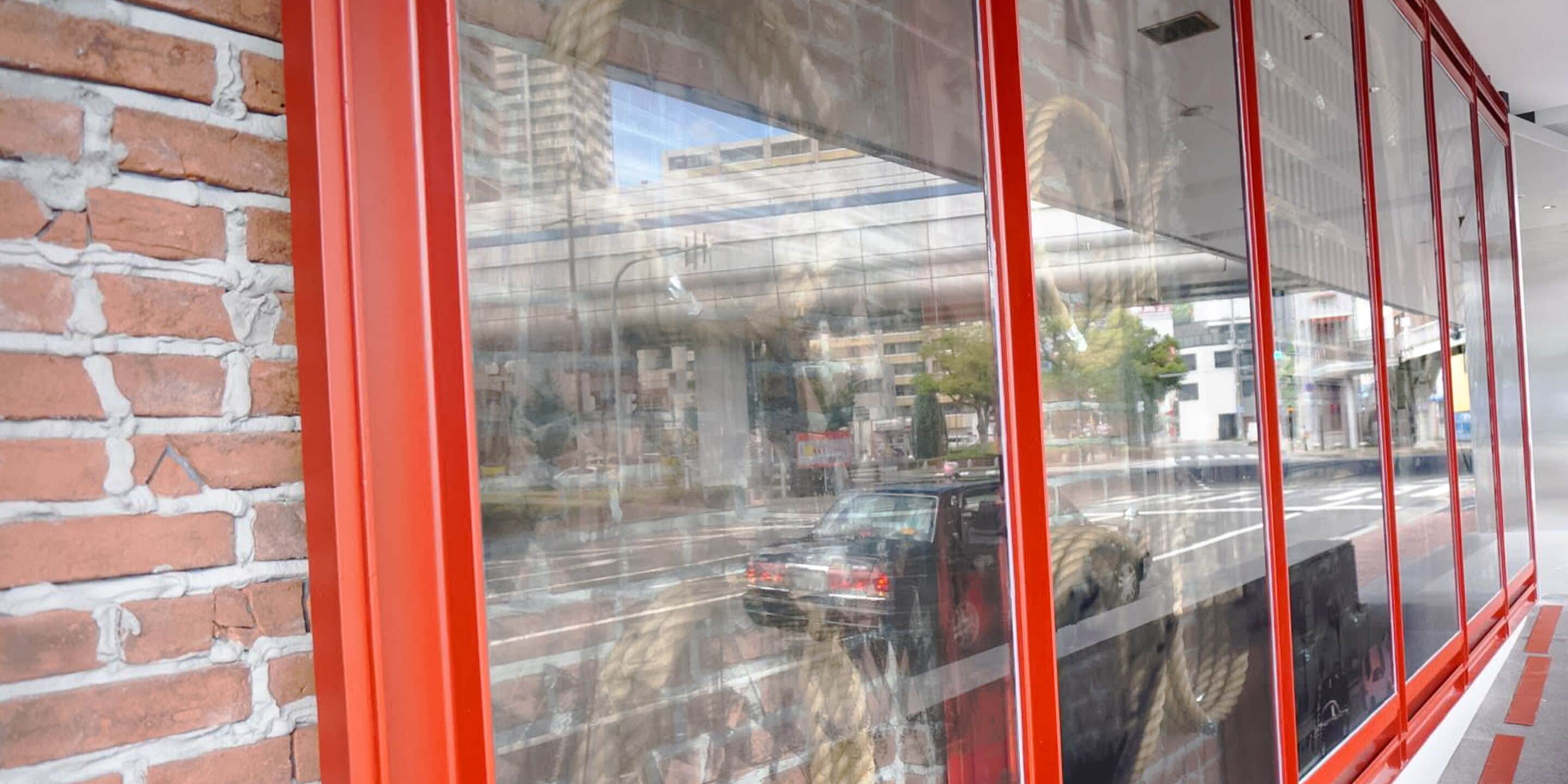 A view through a window with a red frame, reflecting a street scene with cars and buildings.