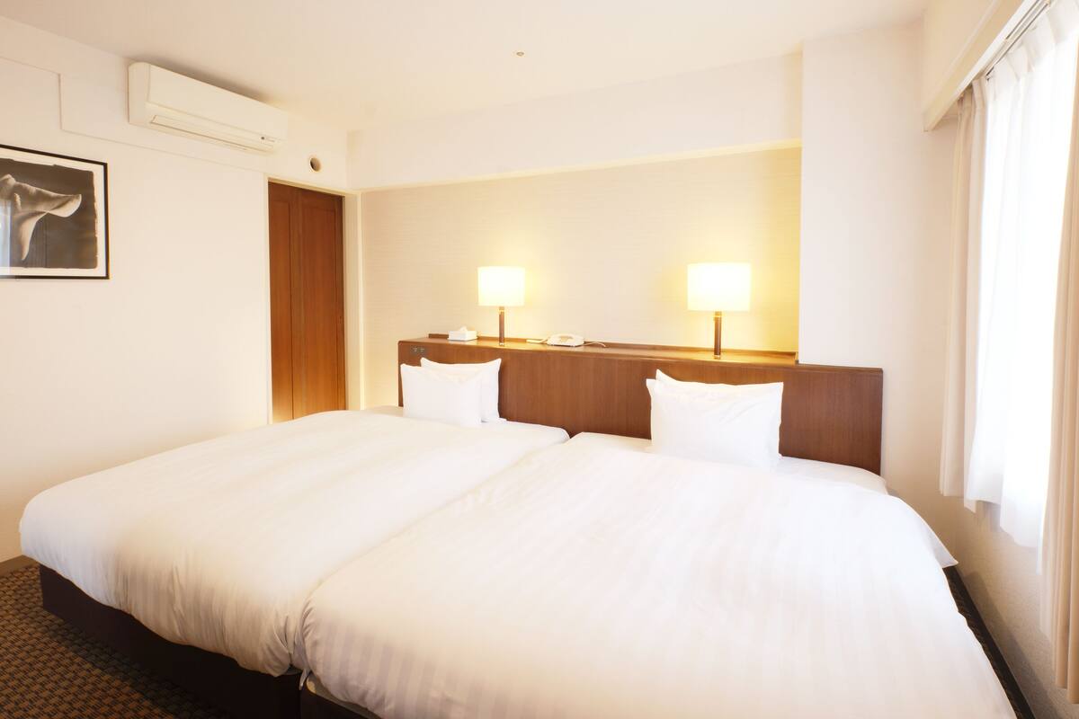 Habitación de hotel con una cama grande, dos lámparas de noche, cabecera de madera, un cuadro en la pared y un equipo de aire acondicionado.