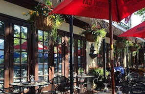 Enjoy meals in a bright and airy outdoor dining area with large windows, rustic wooden beams, and lush greenery.