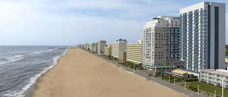 A beachfront hotel with multiple floors, a sandy beach, and a pier in the background.