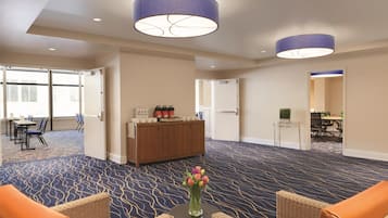 Un hall de hotel con alfombra estampada, muebles de mimbre, un mostrador de recepción y un jarrón de flores.