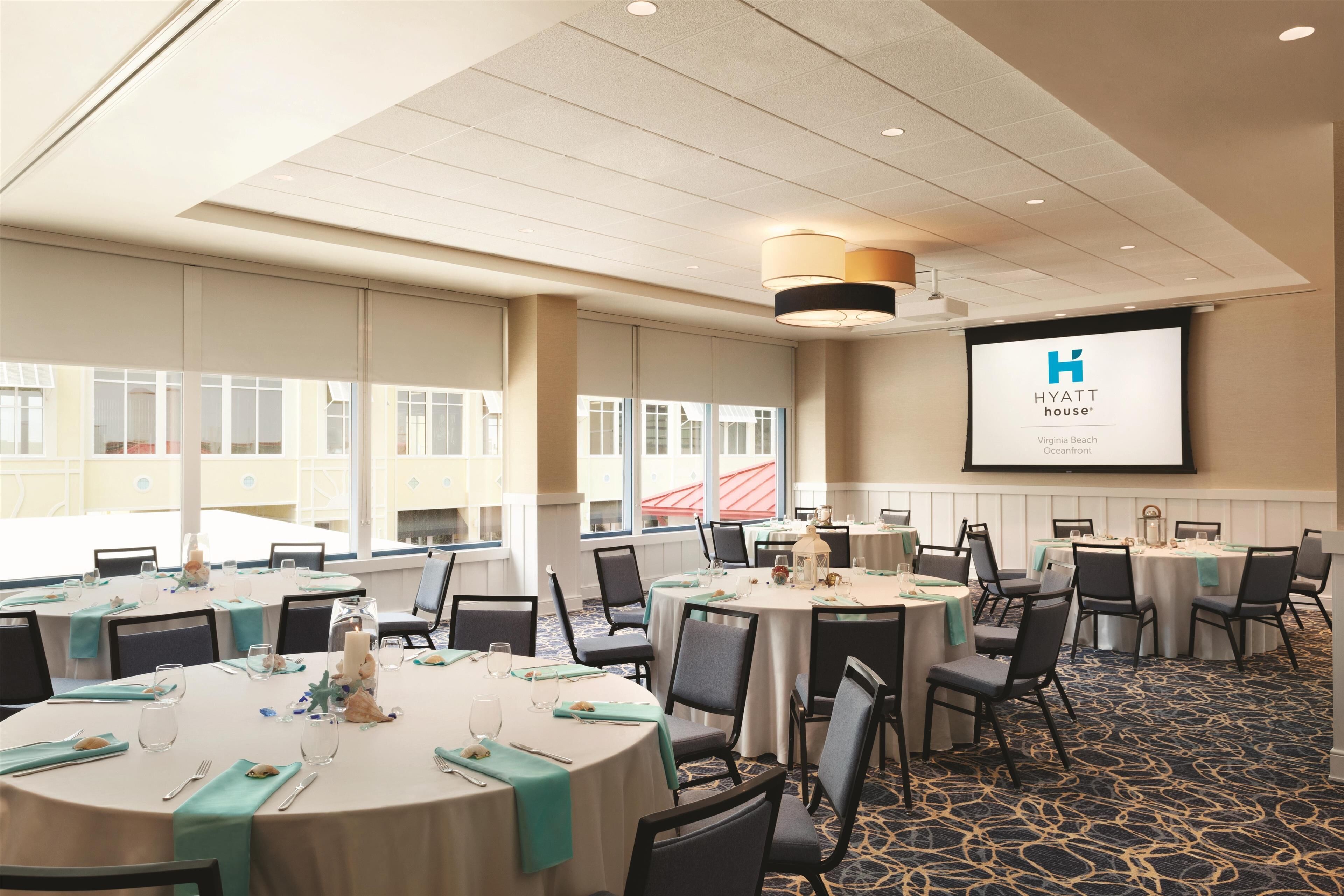 Une salle de conférence équipée de tables rondes, de chaises et d’un écran de projection affichant le logo de Hyatt House.