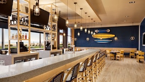 A bar area with a long counter, wooden chairs, and surfboards on the wall. - Hyatt House Virginia Beach / Oceanfront (Virginia Beach)