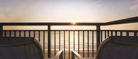 A balcony with two chairs facing a sunset over the ocean.
