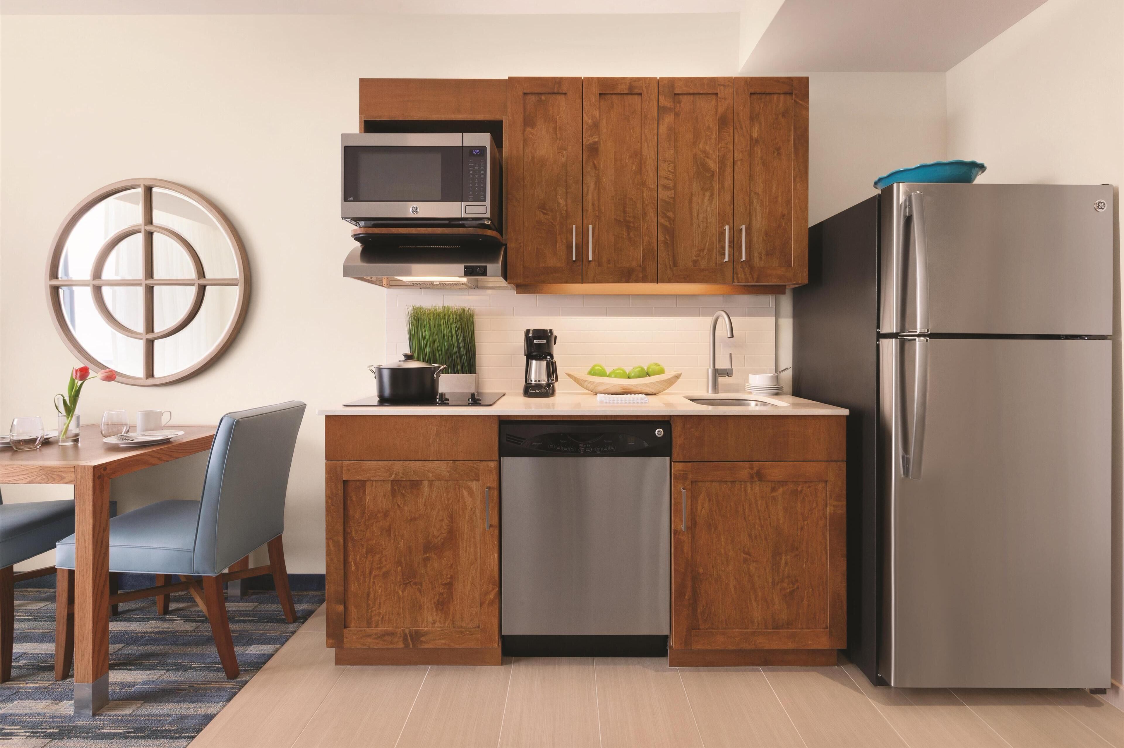 Eine moderne Küche mit Holzschränken, einem Edelstahlkühlschrank, einer Mikrowelle und einer Kaffeemaschine.