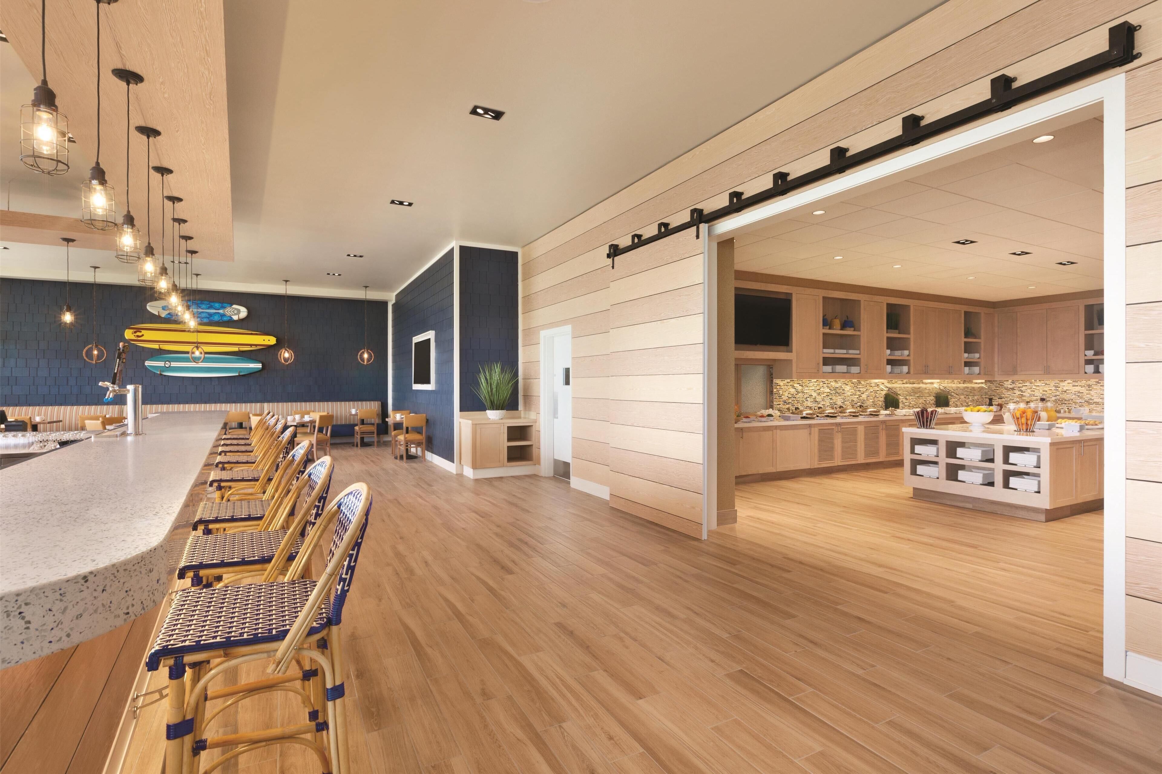 Un moderno vestíbulo de hotel con zona de bar, suelo de madera y una cocina visible a través de un arco.