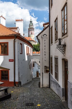 A narrow cobblestone street with historic buildings, a prominent tower in the background, and a sign for Hotel Peregrin. - Hotel Peregrin (Cesky Krumlov)