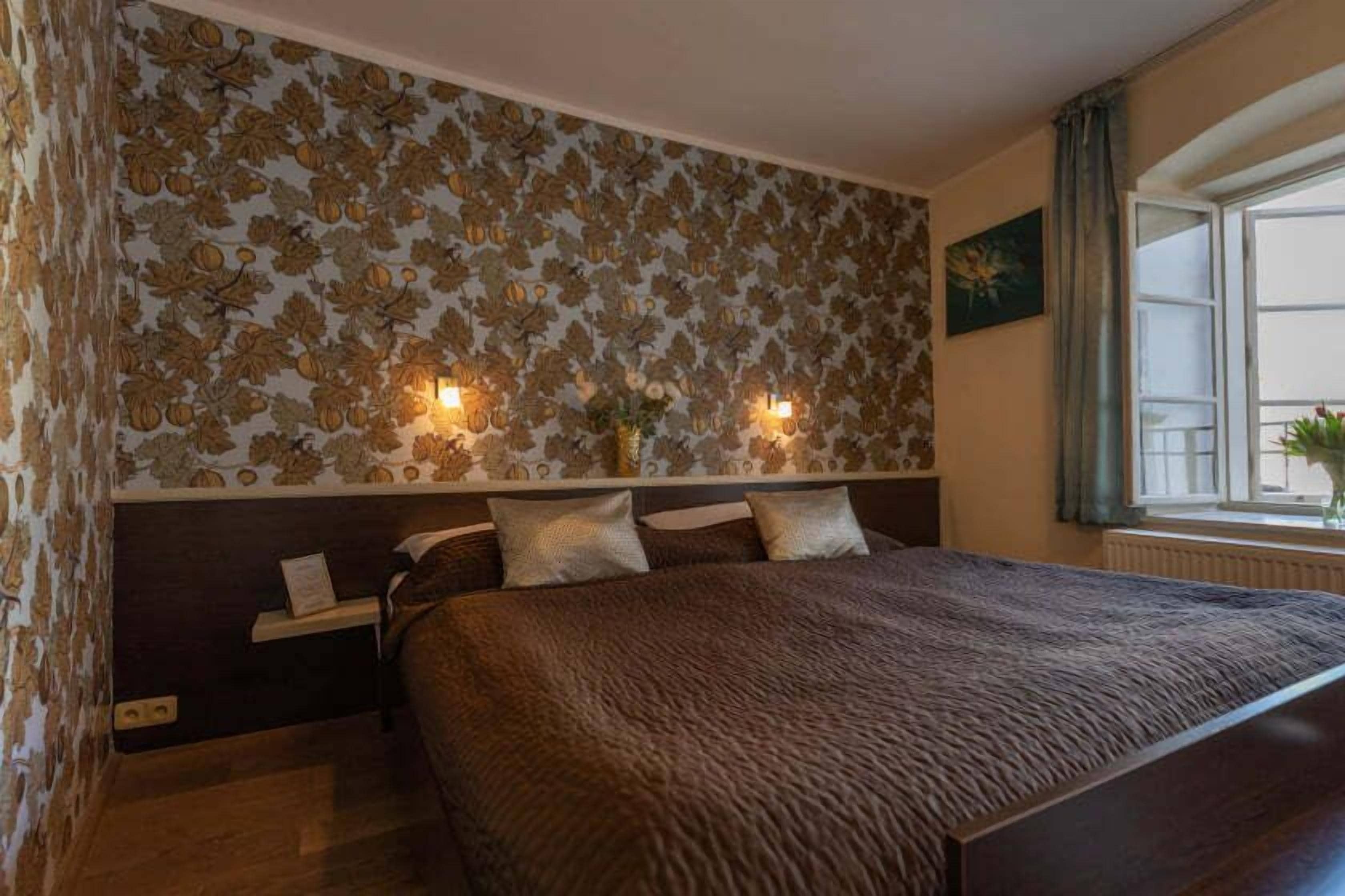 A bedroom with a large bed, a nightstand, two wall-mounted lamps, and a window with curtains.