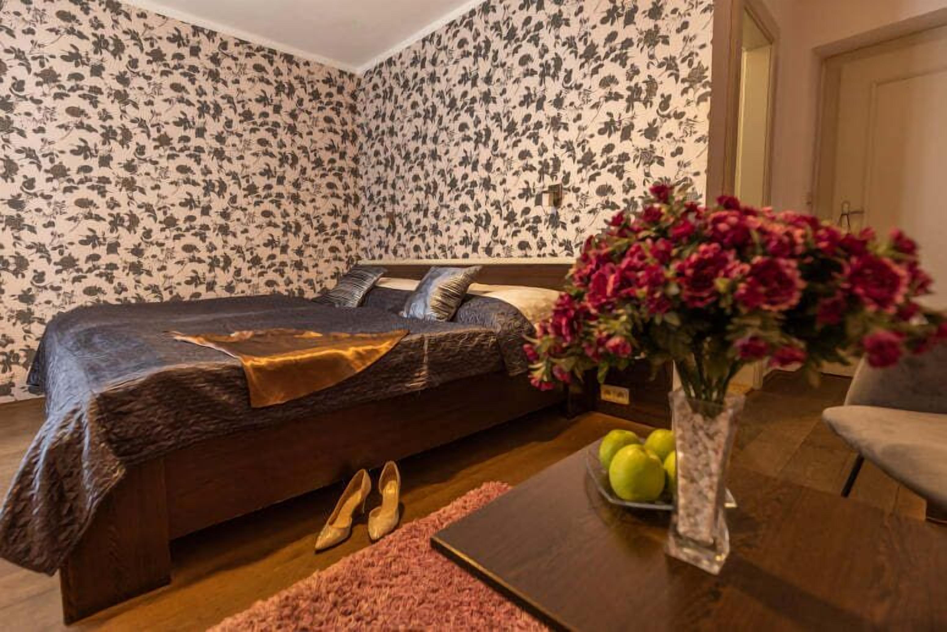 A bedroom with a bed, a vase with flowers, a table with apples, and a pair of shoes.