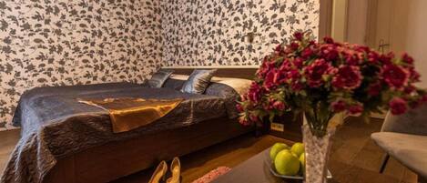 A bedroom with a bed, a vase with flowers, a table with apples, and a pair of shoes.