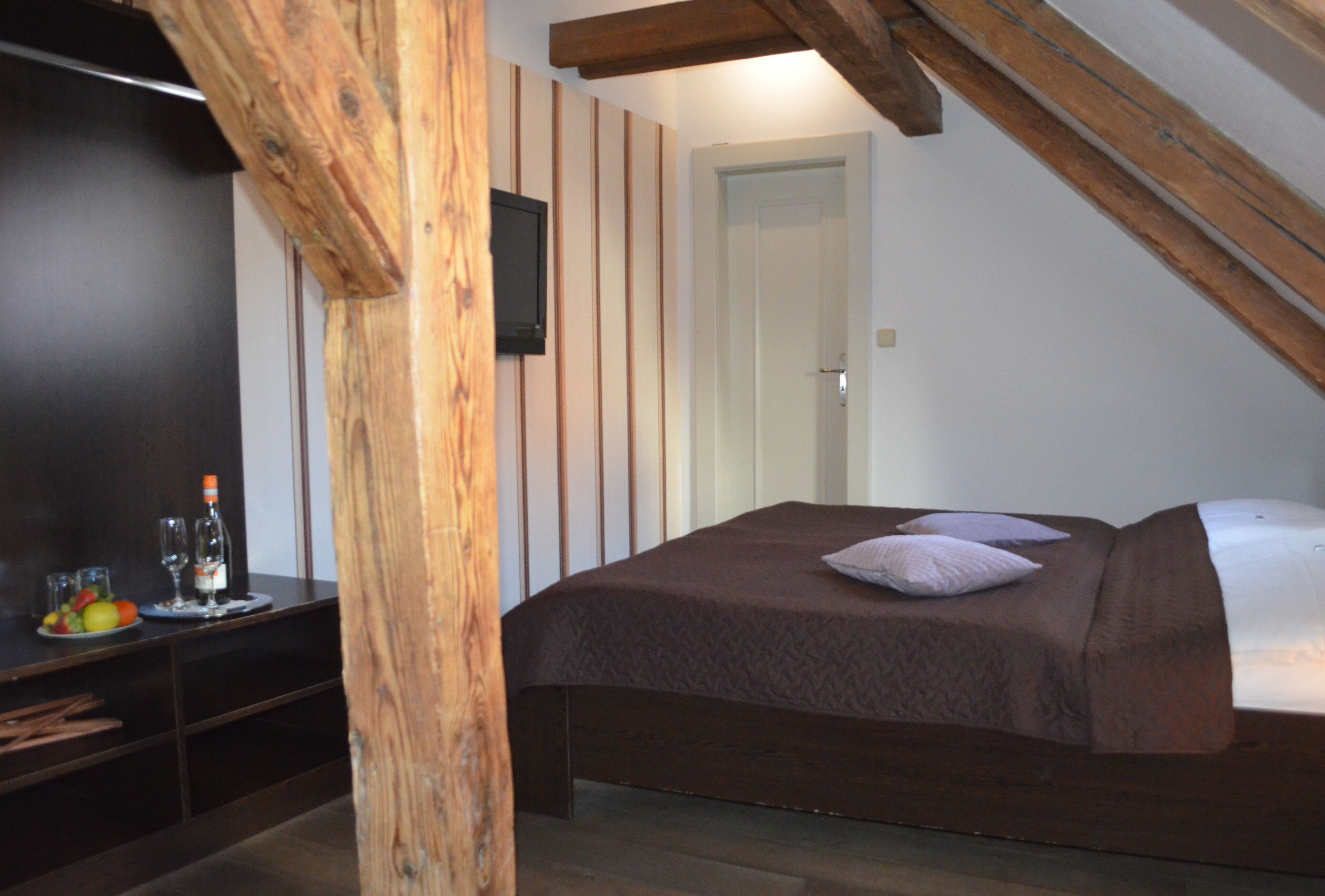 Ein Schlafzimmer mit Holzboden, einem Bett mit brauner Bettdecke, einem Fernseher an der Wand und einer Tür im Hintergrund.
