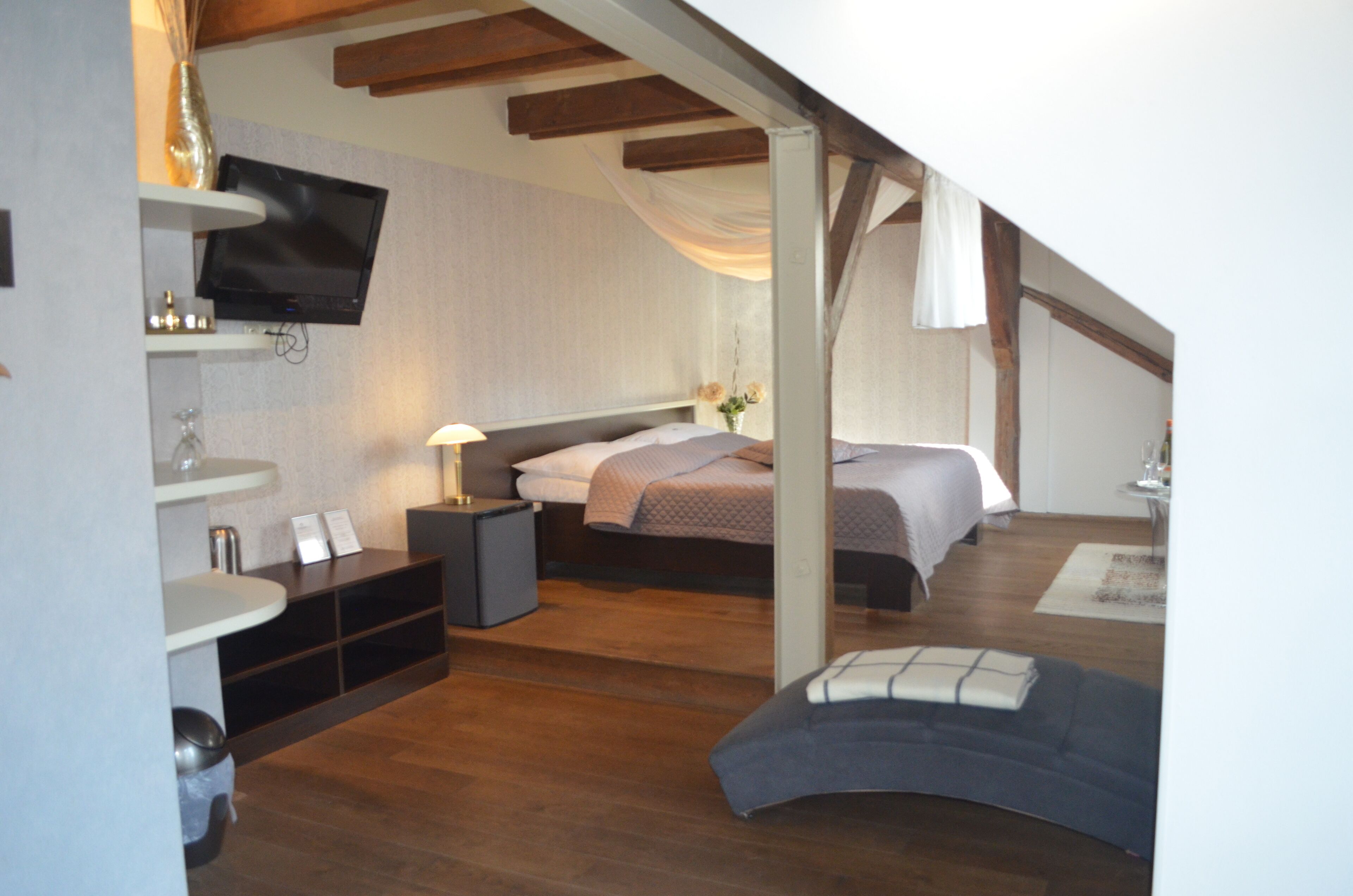 Un dormitorio con cama, mesita de noche, lámpara y televisor montado en la pared.