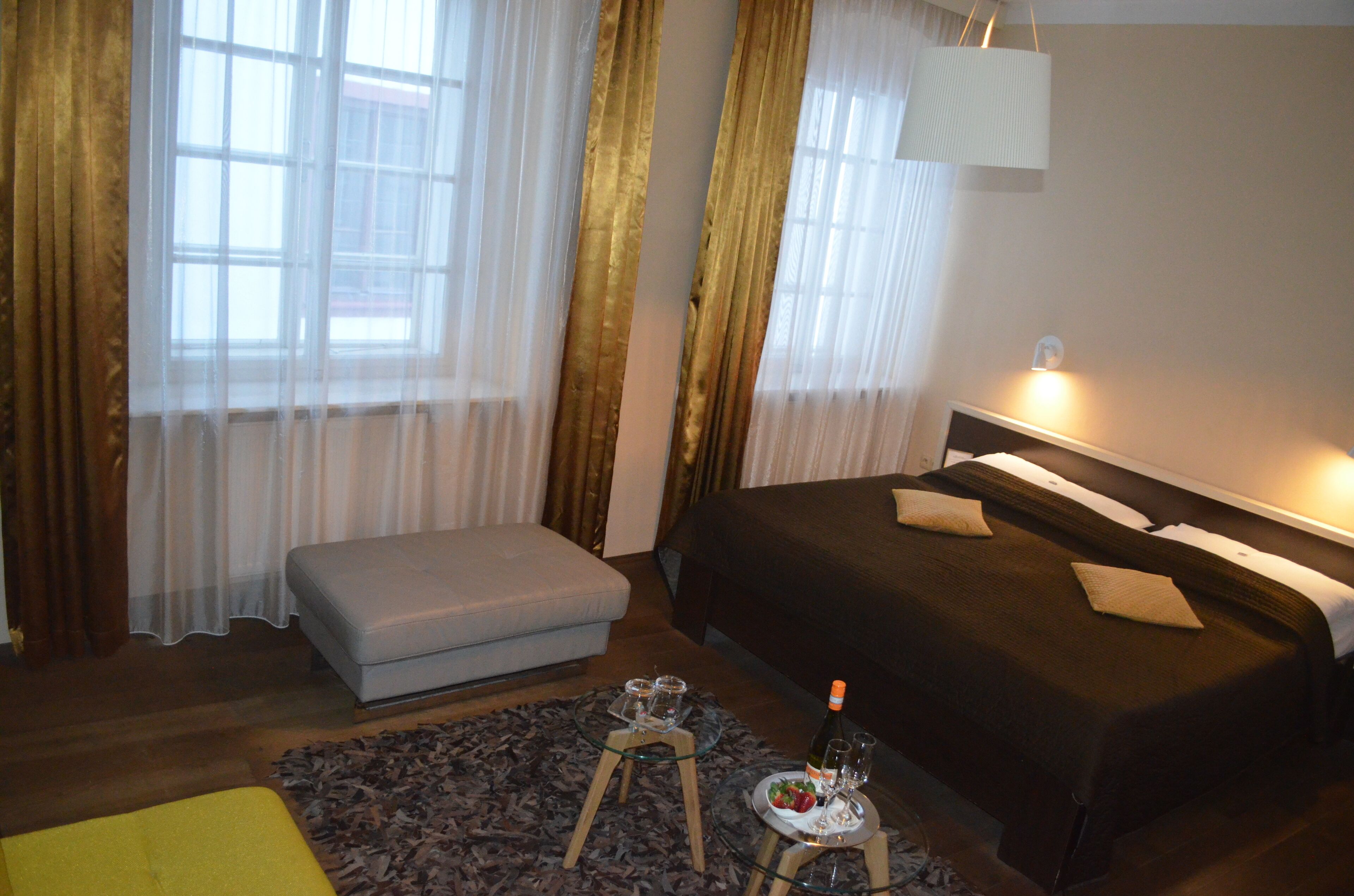 A hotel room with a bed, a small seating area, a table with a tray of food and drinks, and curtains.