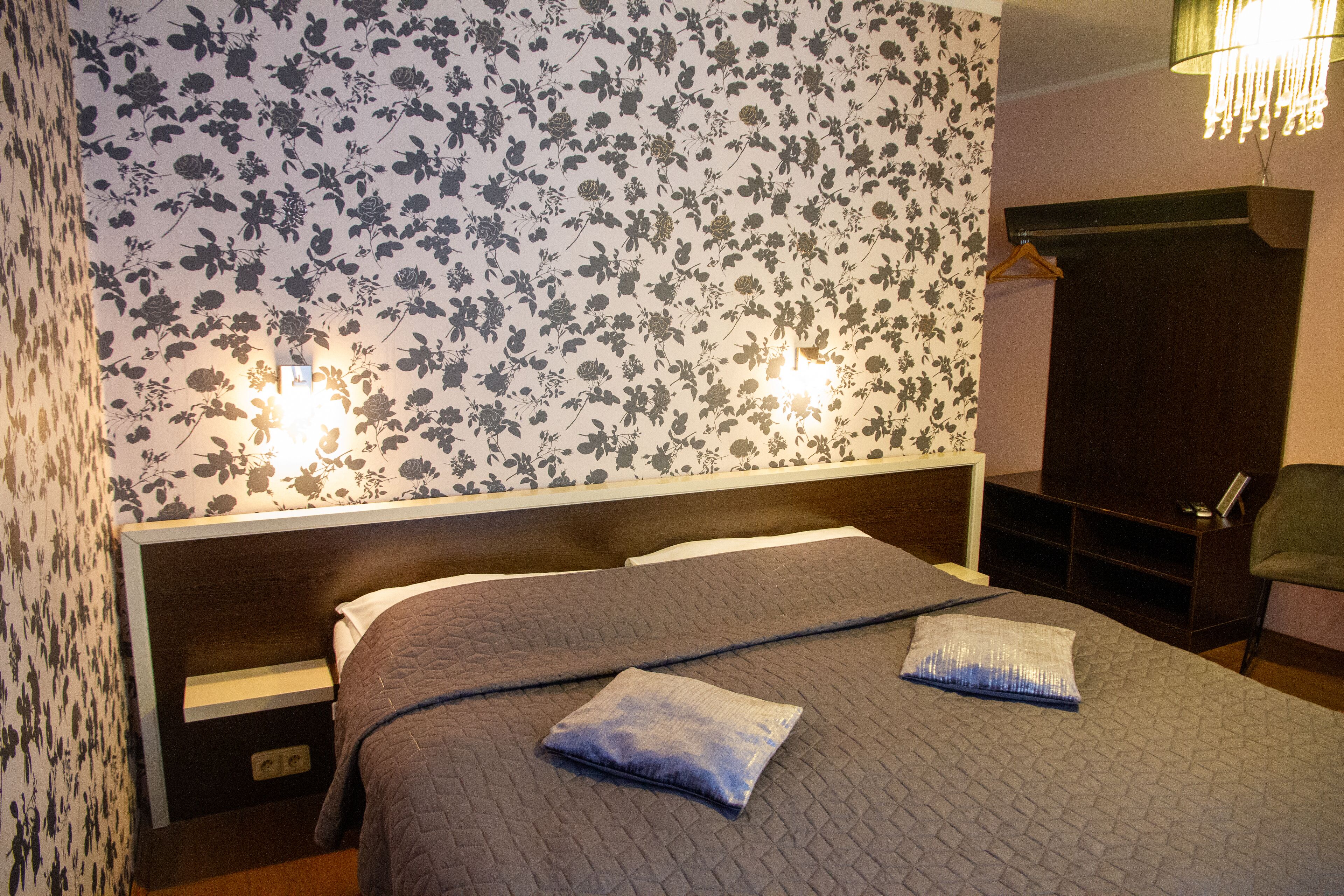 Un lit bien fait, recouvert d’une courtepointe, une table de chevet avec une lampe et une armoire avec un miroir.