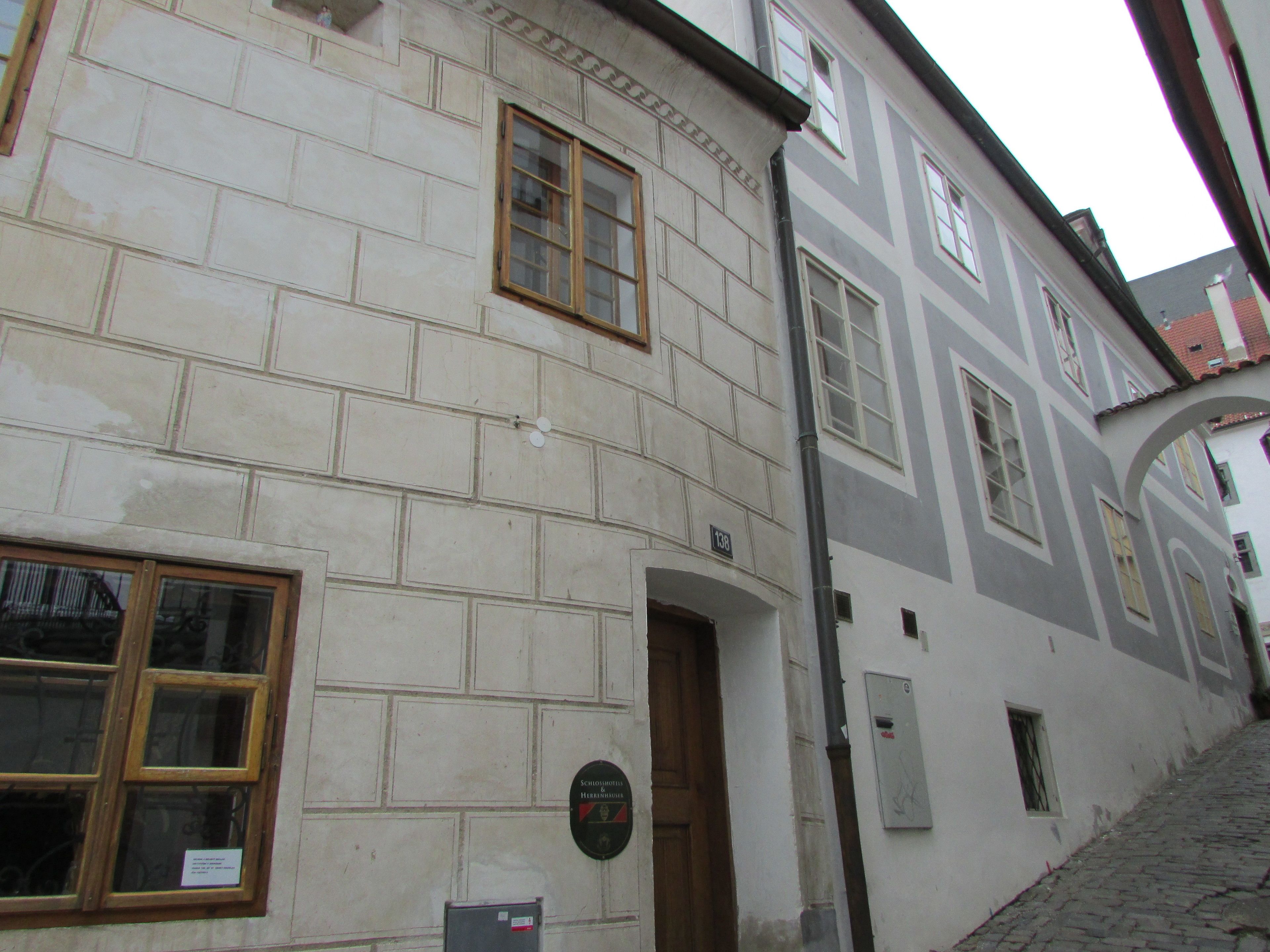 A narrow cobblestone street with a building featuring a traditional facade, a wooden door, and a plaque.