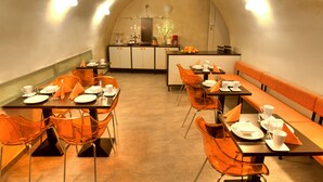 A dining area with tables and chairs, a kitchen in the background, and a bench along the wall. - Hotel Peregrin (Cesky Krumlov)