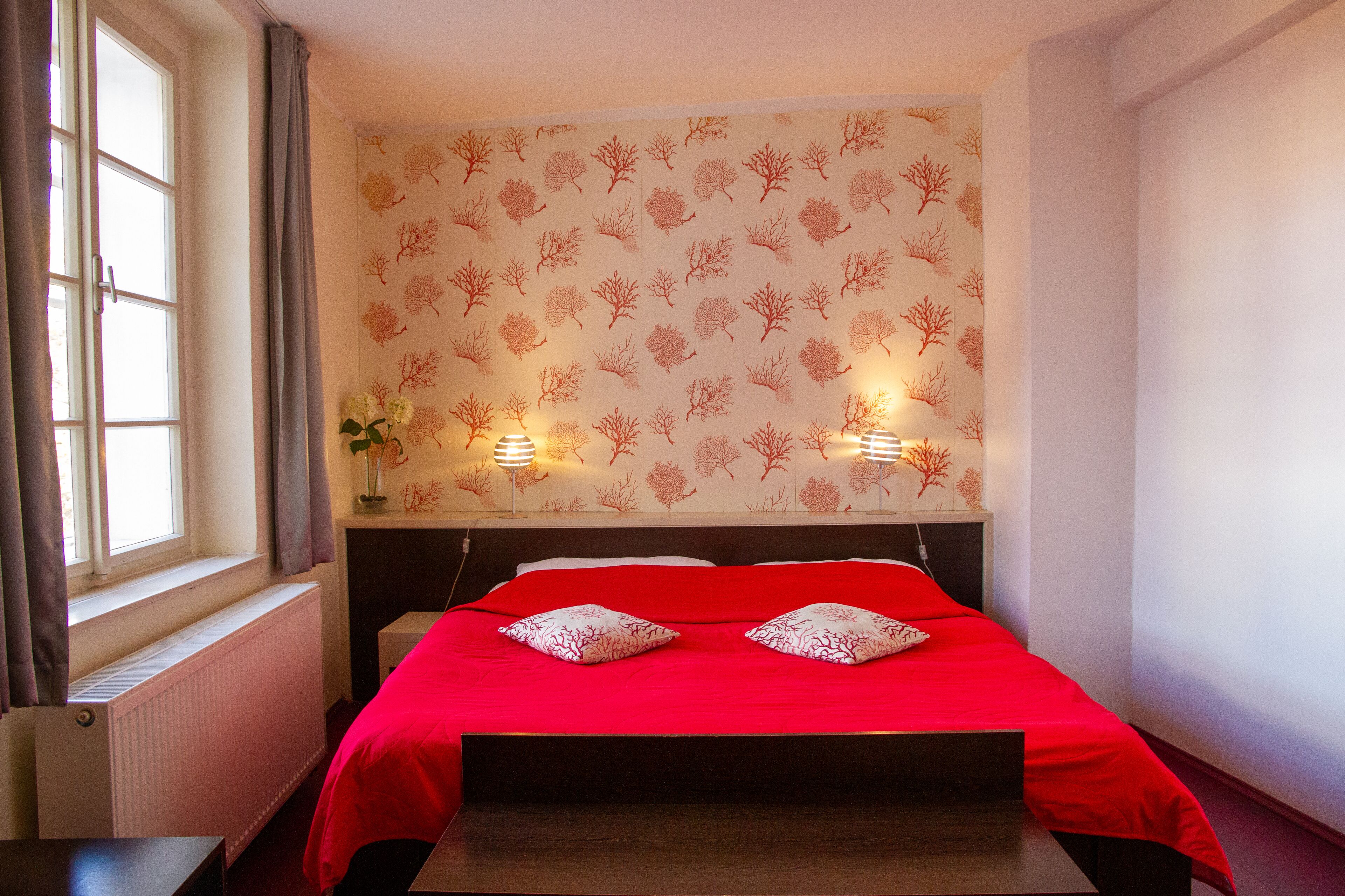 Une chambre d’hôtel avec un lit, deux lampes de chevet, un radiateur et une fenêtre avec des rideaux.