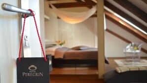A hotel room with a bed, a desk, and a chair. There is a door with a keycard holder and a red rope. - Hotel Peregrin (Cesky Krumlov)