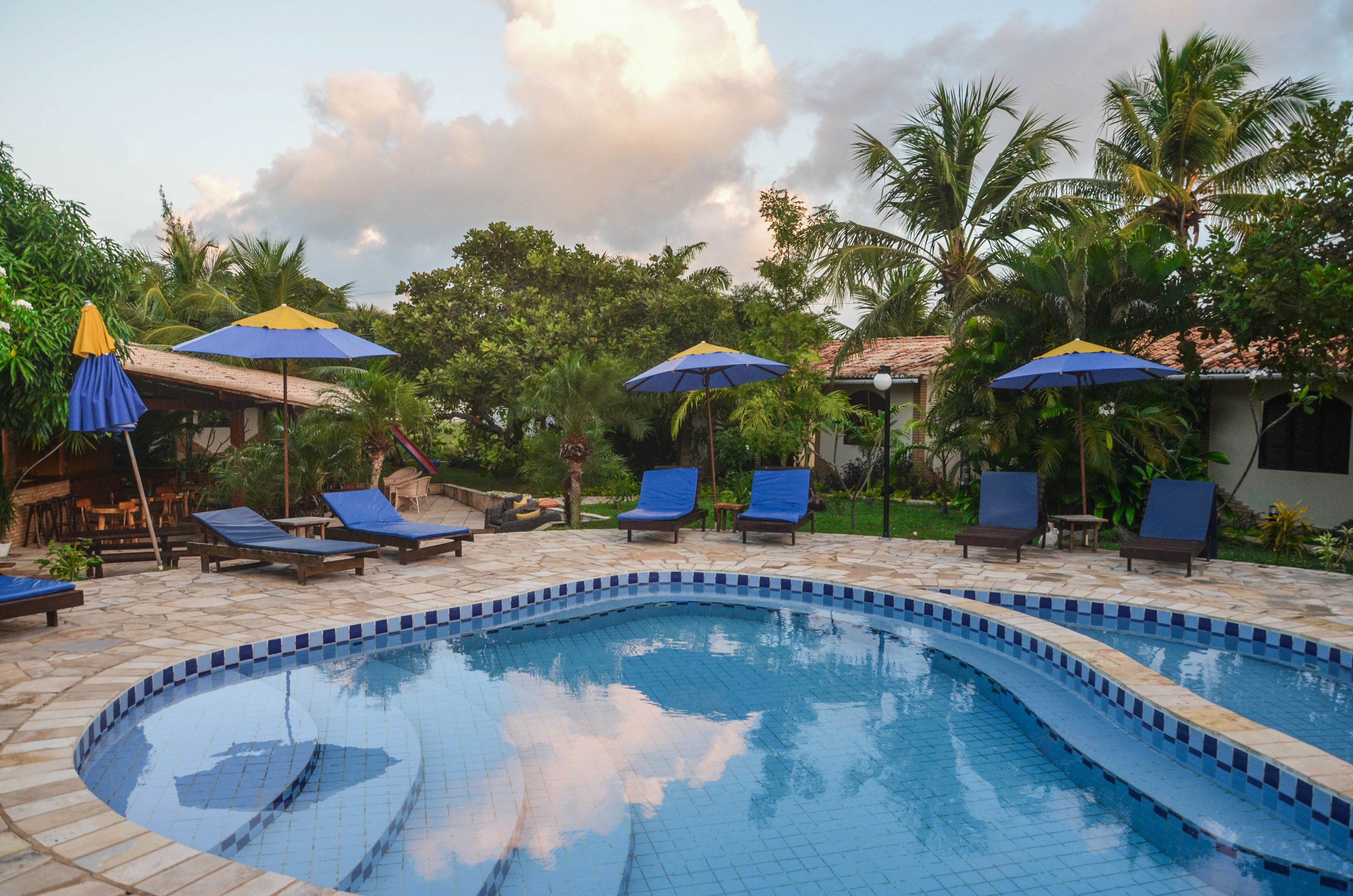 A swimming pool with blue tiles, surrounded by lounge chairs and umbrellas.