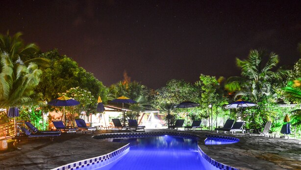 Area piscina illuminata di notte con sedie a sdraio e ombrelloni.
