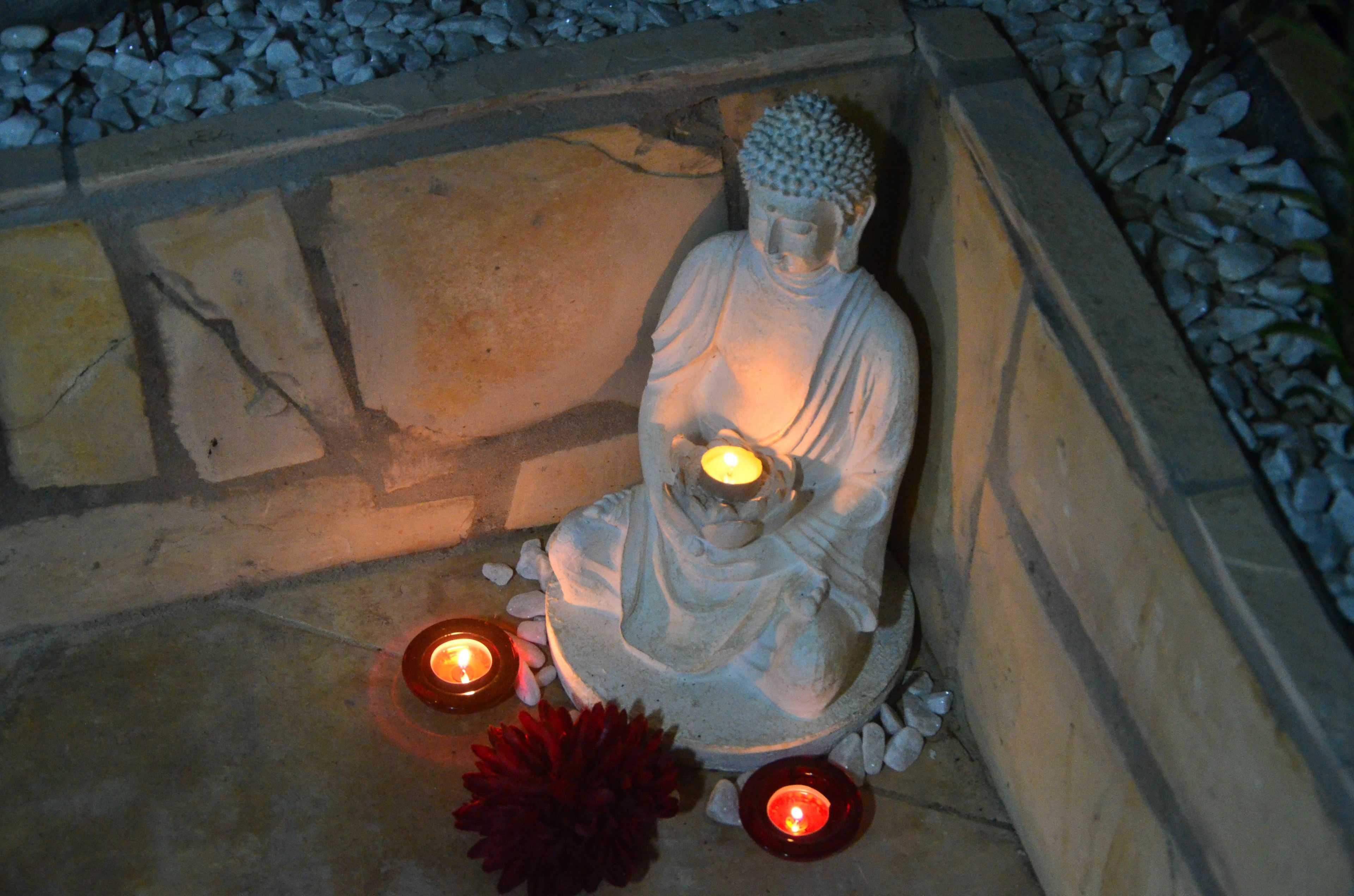 Una estatua de Buda de piedra con dos velas encendidas en primer plano.