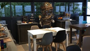 Zona pranzo moderna con tavoli e sedie, un elemento decorativo al centro e vista su piante verdi all'esterno.