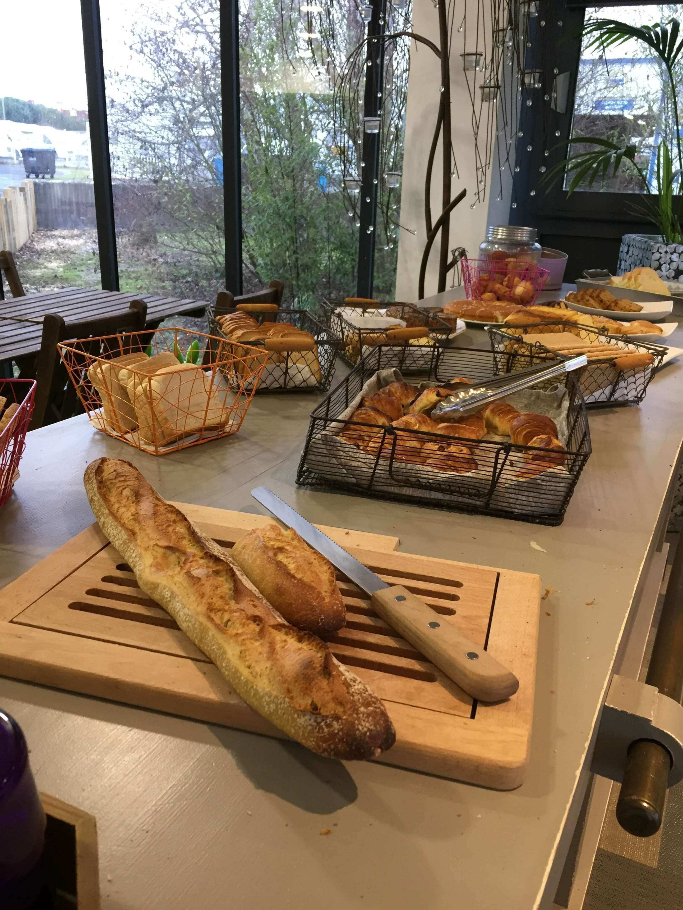 Un comptoir de boulangerie où sont exposés différents types de pains et de viennoiseries, une planche à découper avec un couteau, et des paniers remplis de pain.