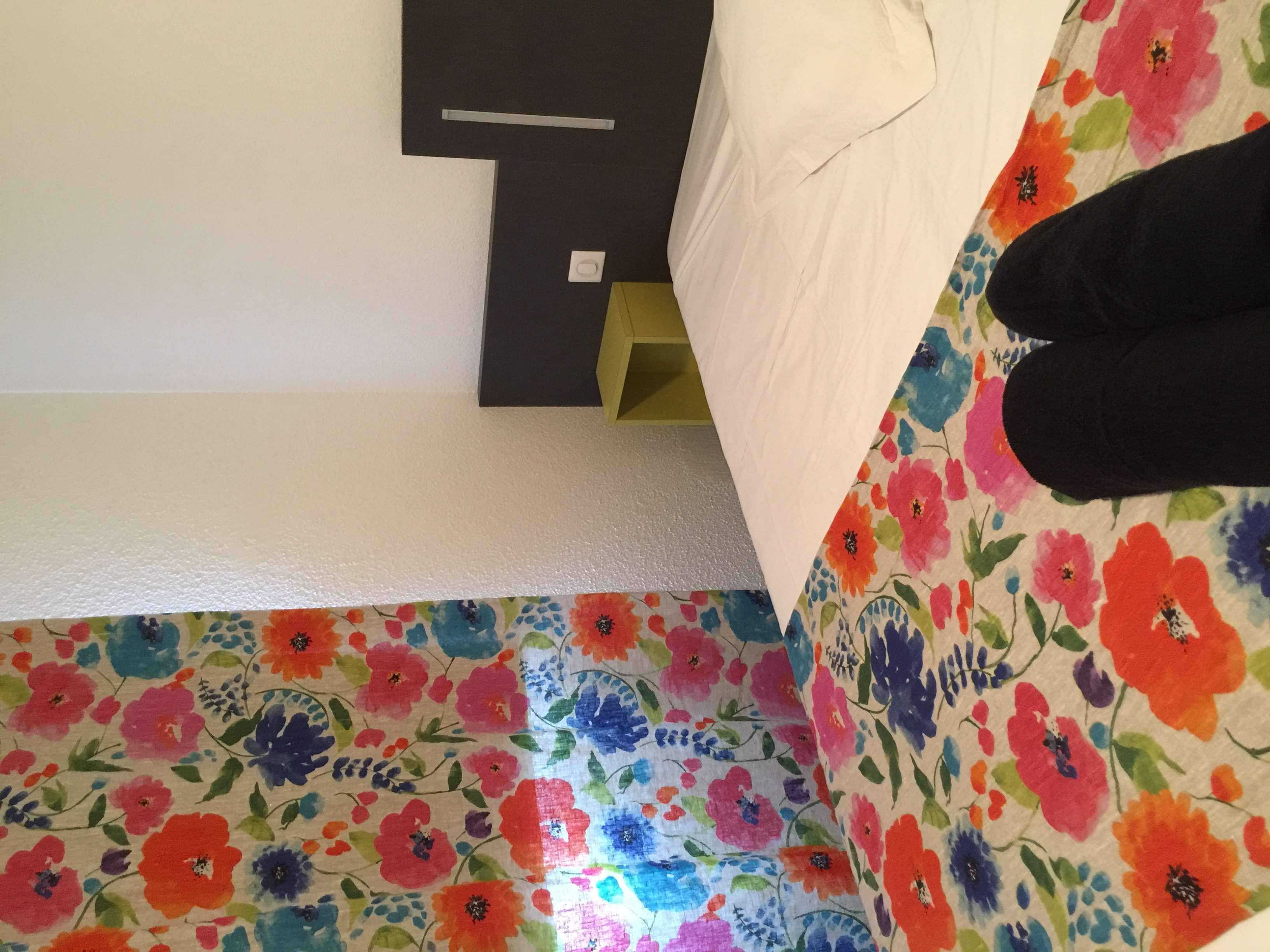 A room with a bed, a nightstand, and a floral-patterned floor.